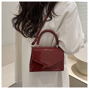 Model view of burgundy patent leather square handbag with golden hardware and shoulder strap