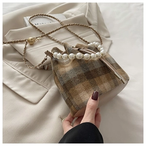 Detail of plaid bucket bag with pearl handle and metal chain strap in warm lighting