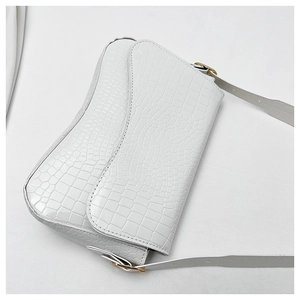 Detail of white crocodile pattern saddle bag with gold buckle on adjustable shoulder strap