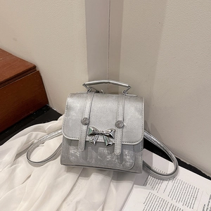 Silver metallic bow backpack with top handle and adjustable straps in a minimalist setting