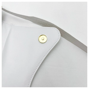 Detail shot of a white leather bag featuring a gold magnetic clasp and croc-embossed strap