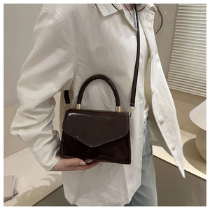 Detail of dark brown patent leather crossbody bag with glossy finish and gold hardware