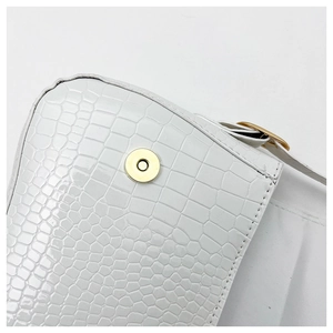 Detail of white crocodile texture leather and round gold magnetic buckle on bag