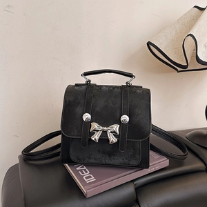 Vintage black bow backpack with silver rivets displayed on a purple book prop