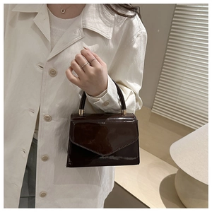 Detail of glossy brown patent leather handbag with envelope flap and round handle