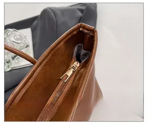 Detail view of smooth golden zipper closure on brown leather tote bag with gray lining