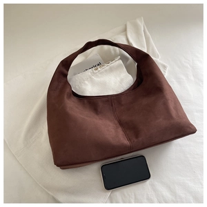 Detail view of large dark brown suede hobo bag shown with a phone for size scale