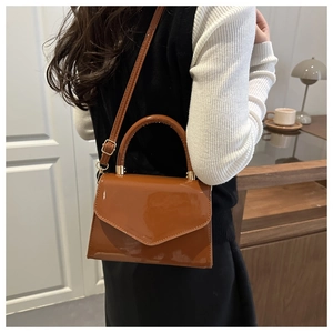 Detail of glossy brown patent leather crossbody bag with top handle and gold hardware