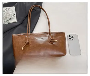 Detailed view of brown leather tote bag size comparison with a mobile phone and knot detail
