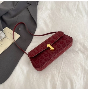 Detail of burgundy leopard print baguette bag with gold twist lock on white fabric