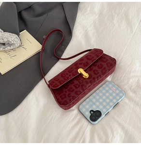 Detail of burgundy leopard print underarm bag with gold metal buckle on soft white fabric