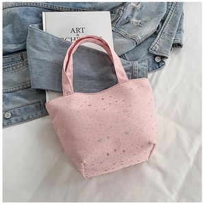 Detail of pink canvas tote bag featuring silver star patterns and bow design on bed