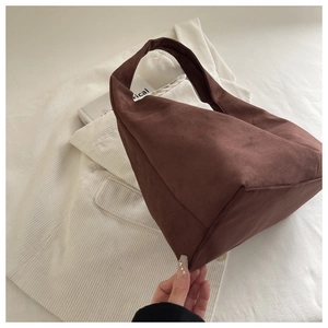 Detailed close-up of dark brown matte suede shoulder bag on soft white fabric background