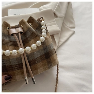 Detail of plaid bucket bag featuring pearl handle and woven chain strap with drawstring