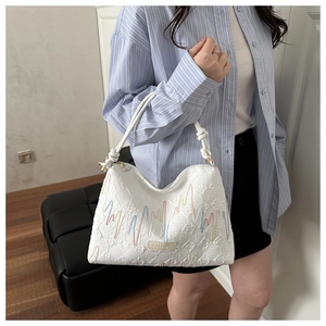Detail of white canvas tote featuring colorful embroidery and relief texture strap