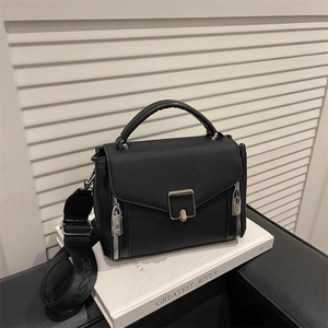 Chic black PU leather handbag with wide logo strap on white book, minimalist studio shot