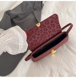 Macro view of burgundy leopard embossed flap bag with gold clasp and interior space