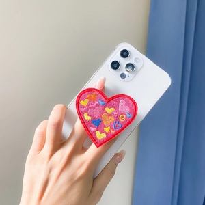 Detail of pink embroidered heart phone grip showing texture and colors on a white phone