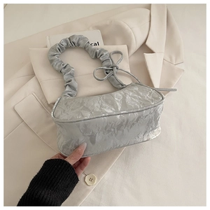 Macro detail of metallic silver pleated fabric and delicate bow on the shoulder bag