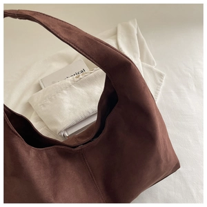 Close-up of deep brown suede shoulder bag with wide strap on a textured white fabric