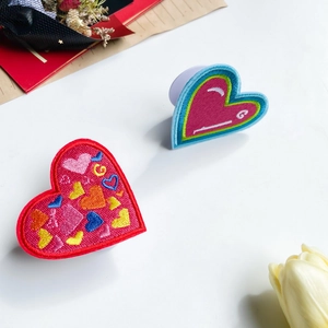 Charming embroidered heart phone socket stands with colorful patterns on white surface