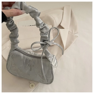 Detail of silver metallic cloud bag featuring ruched handle and metal bow decoration