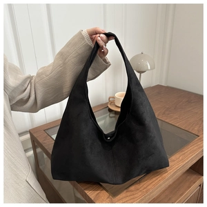 Close-up of black matte hobo bag in soft suede-like texture held by hand in home setting