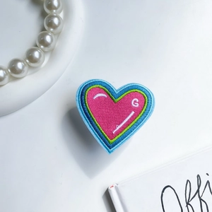 Detail shot of heart-shaped embroidered phone grip with vibrant multi-color stitching
