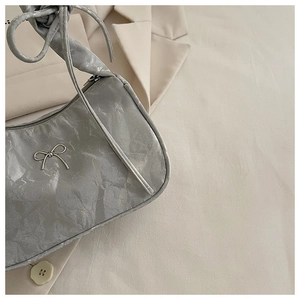 Detailed macro view of silver metallic pleated fabric and chic metal bow on underarm bag