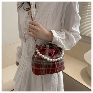 Detail of red plaid bucket bag featuring pearl top handle and chain shoulder strap