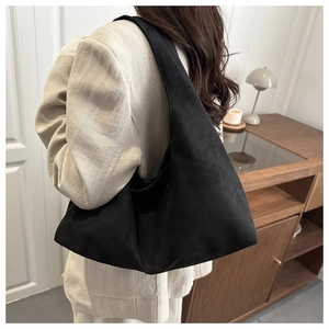 Model wearing a large black matte shoulder bag with a minimalist triangular silhouette