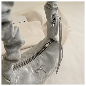 Close-up of ruched silver handbag featuring a metallic bow and elegant cloud-shaped handle