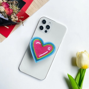 Close-up of pink heart-shaped embroidered phone grip with letter G on white smartphone