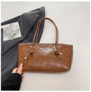 Détail de la poignée nouée et des ferrures dorées sur un sac fourre-tout marron minimaliste
