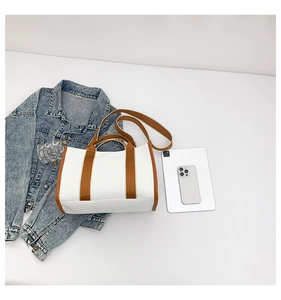 Flat lay of canvas tote bag with brown leather trim next to a tablet and jacket