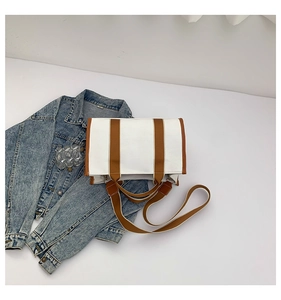 Detail shot of white canvas tote bag with brown straps on a blue denim background