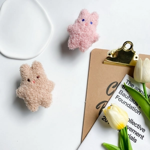 Detailed view of plush bunny phone grips in pink and beige wool texture on tray
