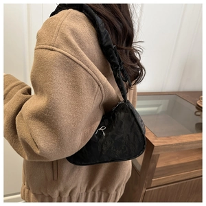 Close-up of black pleated underarm bag featuring a delicate silver metal bow detail