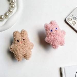 Detail of plush cartoon bunny phone grips in beige and pink curly faux fur texture