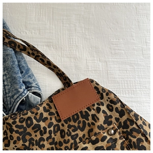 Detail of leopard print canvas tote featuring leather tag and silver metal rivet