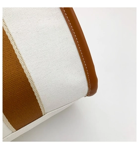 Macro detail of canvas tote bag showing striped texture and brown leather stitching