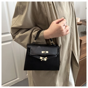 Detail of a black textured leather handbag with gold twist lock on a beige trench coat
