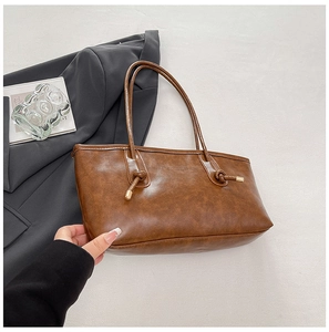 Détail d'un sac cabas en cuir marron avec des anses en corde et des nœuds en métal doré