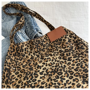 Close-up of leopard print canvas tote bag fabric with brown leather patch and metal rivets