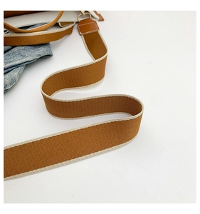 Close-up of tan canvas strap with cream edges and premium gold metal clasps