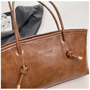 Gros plan du sac cabas marron avec texture cuir, nœud décoratif et détails dorés