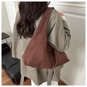 Detail of a large brown suede hobo bag worn by a model in a minimalist setting