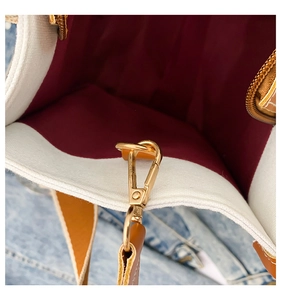 Close-up of golden metal clasp with wine red lining and white canvas bag details
