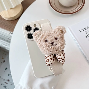 White iPhone case featuring a 3D plush teddy bear with a leopard print bow and wrist strap