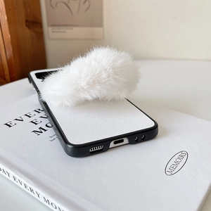Close-up of white textured leather phone case with a large fluffy white faux fur ball charm
